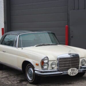 Classic white vintage car parked outside garage.